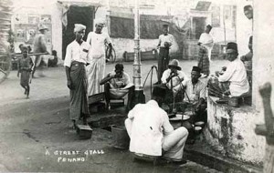 ‘A Street Stall, Penang’ shows customers enjoying Mamak food at a street junction. Nasi kandar, gandum and other ‘mamak’ food used to be sold by itinerant hawkers carrying their food in baskets suspended from shoulder yokes (kandar). Wade Collection.