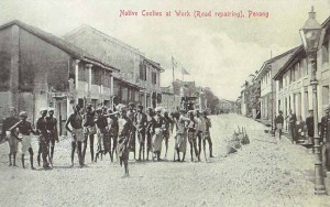 ‘Native Coolies at Work (Road repairing), Penang’. A ‘chain-gang’ of labourers undertaking road repairs on Transfer Road, being watched by their overseers (right) from the colonial public works department. In the background is the Keramat Dato’ Koya, marked by a pair of flags. Wade Collection.